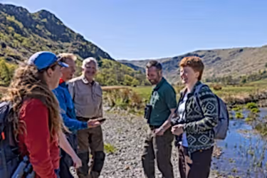 Group of people stood beside a river talking and smiling.