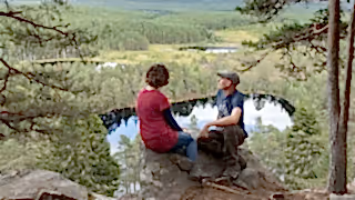 A man and a woman sat on a rock looking out from a scenic viewpoint above Uath Lochans in the Cairngorms National Park